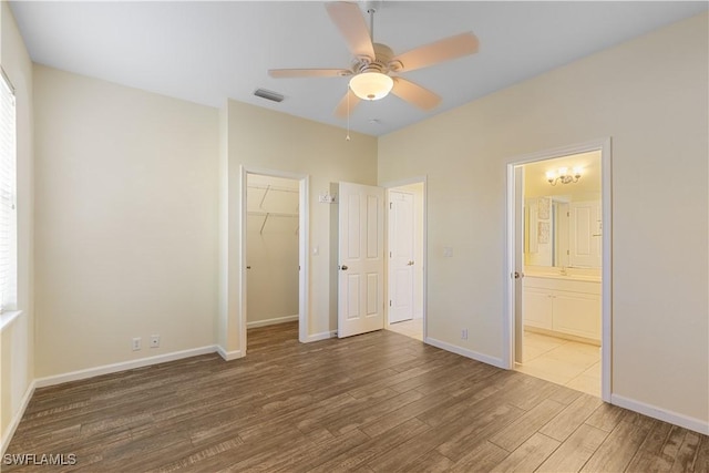 unfurnished bedroom with ensuite bathroom, hardwood / wood-style flooring, a walk in closet, ceiling fan, and a closet