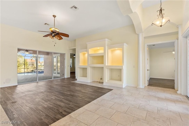 unfurnished living room with built in shelves, ceiling fan, light hardwood / wood-style flooring, and a towering ceiling