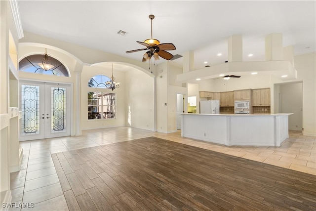 unfurnished living room featuring ceiling fan with notable chandelier, a towering ceiling, french doors, and light wood-type flooring