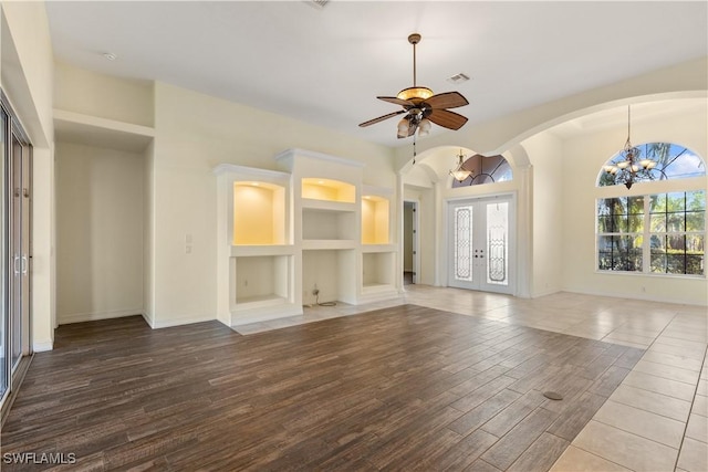 unfurnished living room featuring french doors, wood-type flooring, ceiling fan with notable chandelier, and built in features