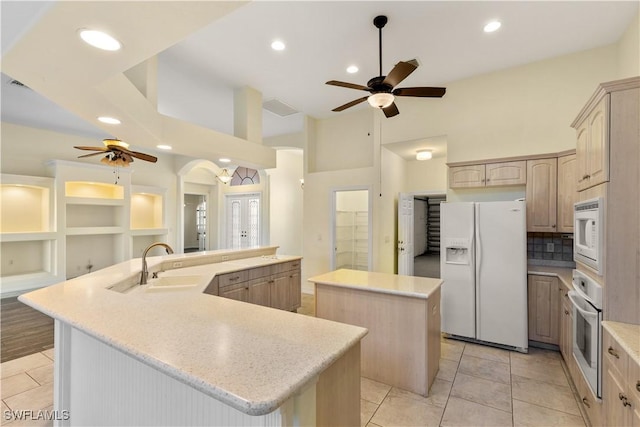 kitchen with ceiling fan, white appliances, sink, and a kitchen island with sink