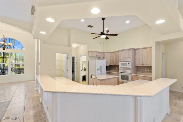 kitchen with ceiling fan with notable chandelier, light brown cabinetry, decorative backsplash, a large island with sink, and white appliances