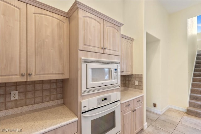 kitchen with tasteful backsplash, white appliances, light tile patterned floors, and light brown cabinets