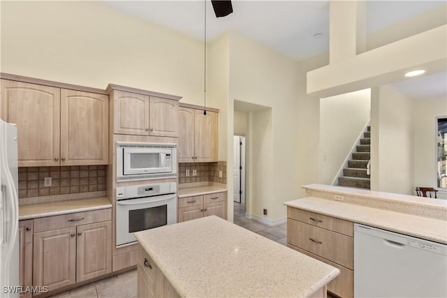 kitchen featuring pendant lighting, white appliances, light brown cabinetry, and backsplash