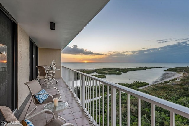 balcony at dusk featuring a water view