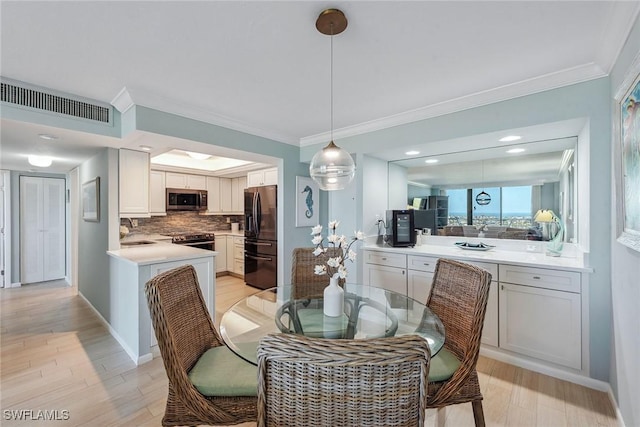 dining area with sink, light wood-type flooring, and ornamental molding