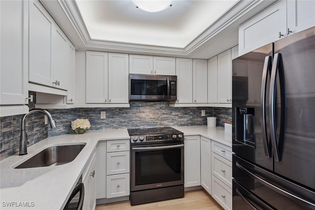 kitchen with white cabinets, stainless steel appliances, a tray ceiling, and sink