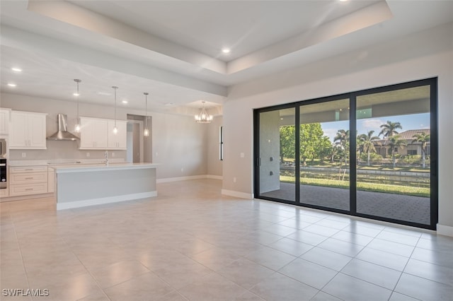 unfurnished living room with an inviting chandelier, light tile patterned floors, sink, and a tray ceiling