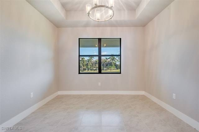 tiled spare room with a chandelier and a tray ceiling