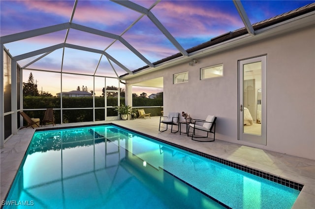 pool at dusk featuring glass enclosure and a patio area