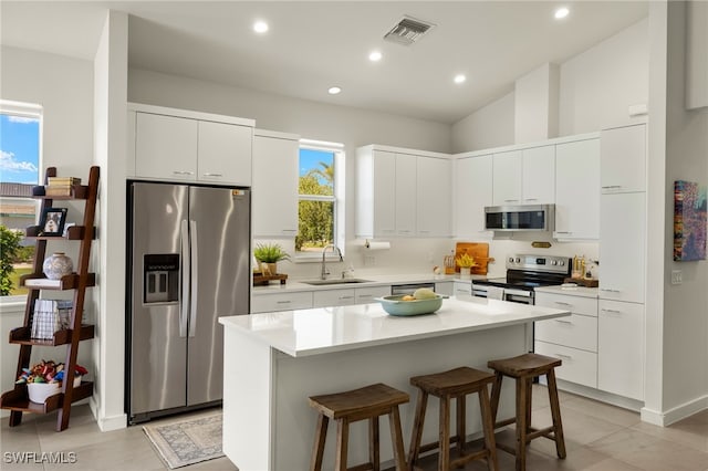 kitchen featuring appliances with stainless steel finishes, a breakfast bar, sink, a center island, and white cabinetry