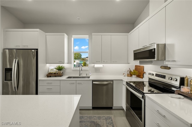 kitchen featuring appliances with stainless steel finishes, light tile patterned floors, white cabinetry, and sink