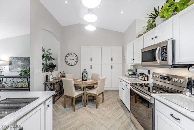 kitchen with stainless steel appliances, white cabinets, vaulted ceiling, decorative backsplash, and light parquet flooring