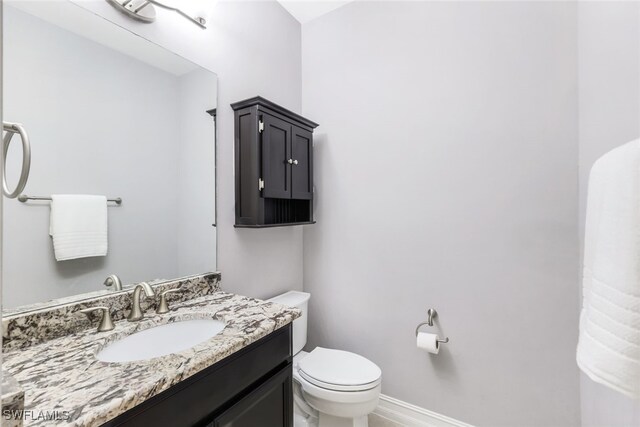 half bathroom with vanity, toilet, and baseboards