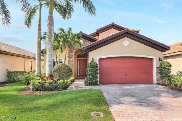 mediterranean / spanish-style house with an attached garage, stone siding, decorative driveway, stucco siding, and a front yard