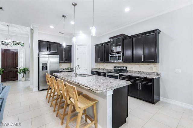 kitchen with stainless steel appliances, a sink, light stone counters, and a center island with sink