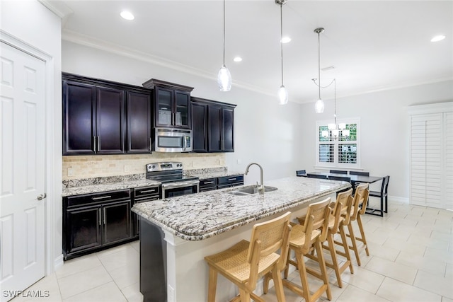 kitchen with a breakfast bar area, stainless steel appliances, hanging light fixtures, a sink, and an island with sink