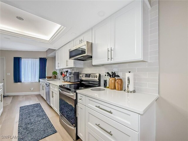 kitchen with backsplash, white cabinetry, stainless steel appliances, and light hardwood / wood-style flooring