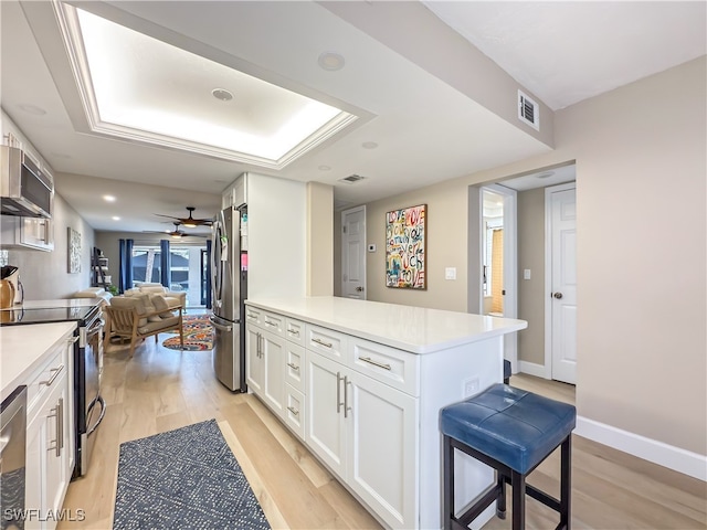 kitchen with white cabinets, a kitchen breakfast bar, ceiling fan, appliances with stainless steel finishes, and light hardwood / wood-style floors