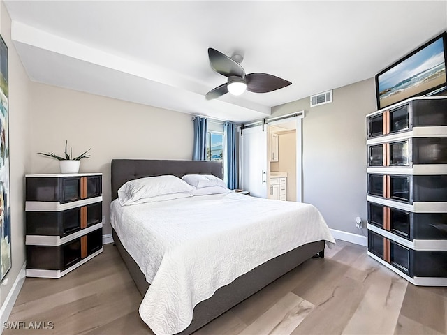 bedroom with hardwood / wood-style flooring, ceiling fan, a barn door, and connected bathroom