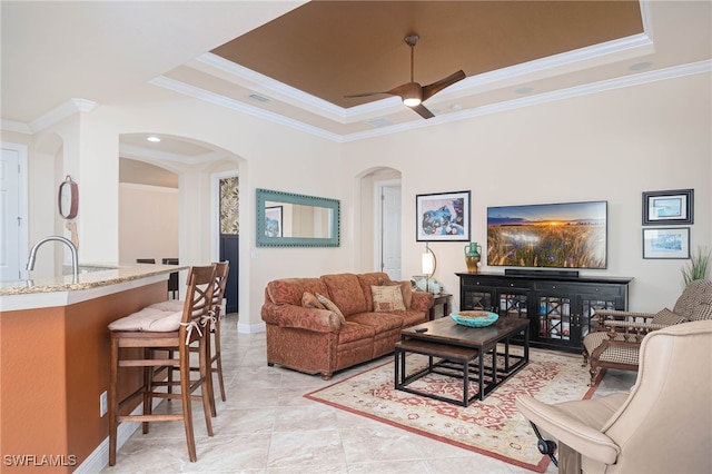 living room featuring a raised ceiling, sink, crown molding, ceiling fan, and light tile patterned floors