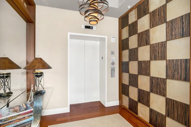 foyer featuring elevator, wood-type flooring, and a notable chandelier