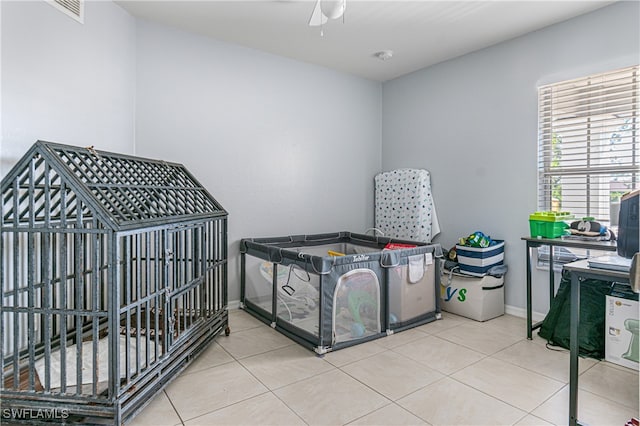 bedroom with light tile patterned floors, a nursery area, and ceiling fan