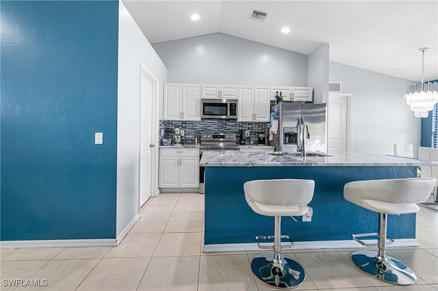 kitchen featuring white cabinets, a center island with sink, vaulted ceiling, decorative light fixtures, and stainless steel appliances