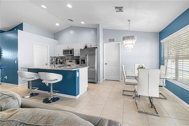 kitchen with stainless steel appliances, an island with sink, pendant lighting, lofted ceiling, and white cabinets