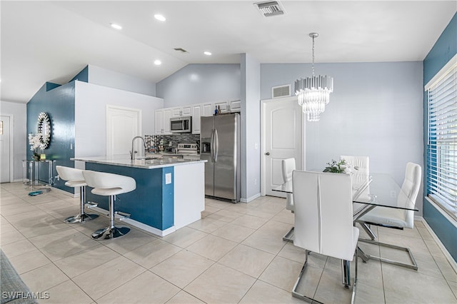 kitchen featuring appliances with stainless steel finishes, a kitchen breakfast bar, vaulted ceiling, pendant lighting, and white cabinets