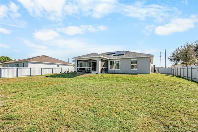 rear view of property with solar panels, a sunroom, and a lawn