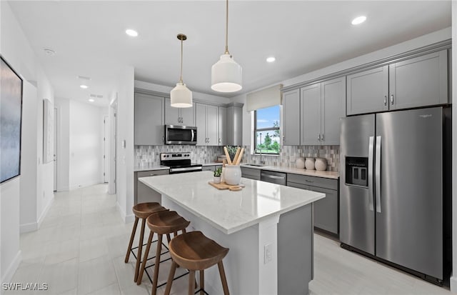 kitchen featuring appliances with stainless steel finishes, backsplash, a kitchen island, gray cabinetry, and pendant lighting