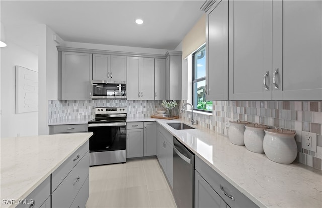 kitchen featuring stainless steel appliances, light tile patterned floors, sink, backsplash, and light stone countertops