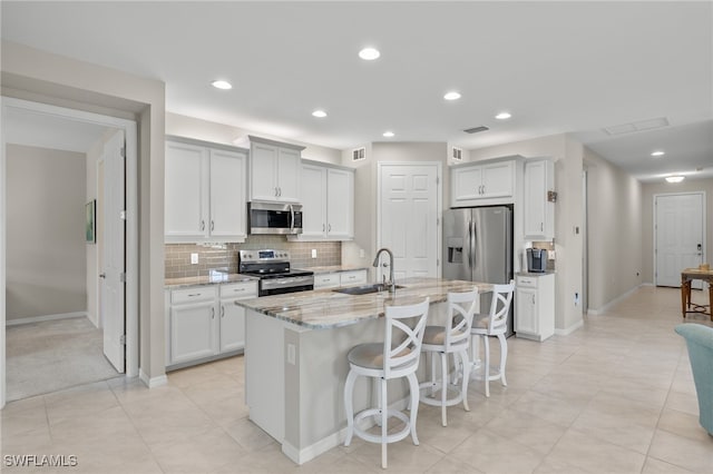 kitchen with light stone countertops, sink, stainless steel appliances, an island with sink, and a breakfast bar