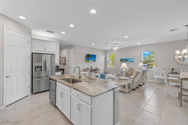 kitchen with light stone counters, stainless steel appliances, sink, a center island with sink, and white cabinetry