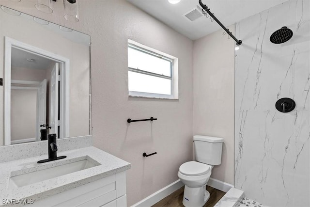 bathroom with hardwood / wood-style flooring, vanity, toilet, and tiled shower