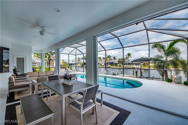 view of pool featuring outdoor lounge area, ceiling fan, glass enclosure, a water view, and a patio