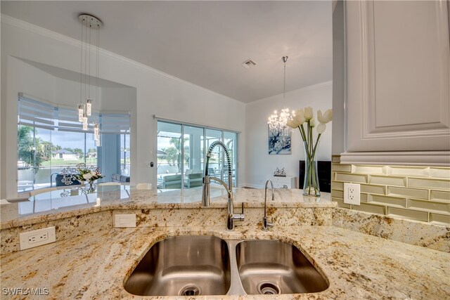 kitchen with pendant lighting, light stone counters, crown molding, and sink