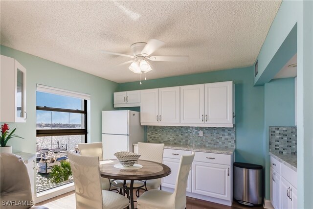 kitchen with decorative backsplash, light stone countertops, light wood-type flooring, white refrigerator, and white cabinets