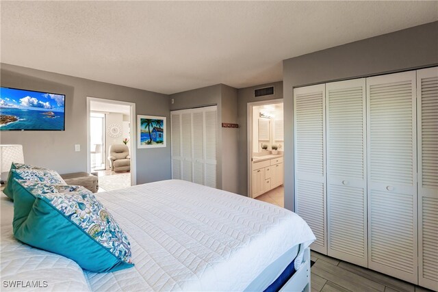 bedroom with a textured ceiling, light wood-type flooring, ensuite bath, and multiple closets