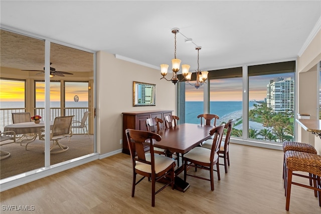 dining room featuring light wood-style flooring, a water view, baseboards, ceiling fan with notable chandelier, and ornamental molding