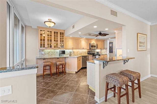 kitchen featuring a breakfast bar area, kitchen peninsula, light brown cabinetry, and stainless steel appliances