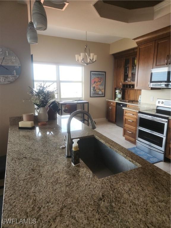 kitchen with stone counters, decorative light fixtures, a sink, appliances with stainless steel finishes, and glass insert cabinets