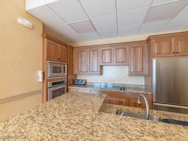 kitchen featuring a paneled ceiling, stainless steel appliances, light stone counters, and backsplash