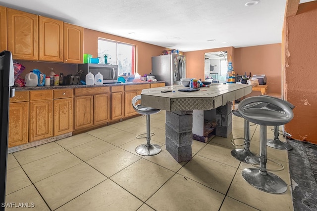 kitchen featuring a kitchen bar, appliances with stainless steel finishes, and light tile patterned flooring