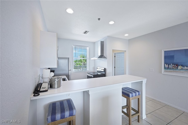 kitchen featuring kitchen peninsula, a breakfast bar area, wall chimney exhaust hood, white cabinetry, and stainless steel appliances