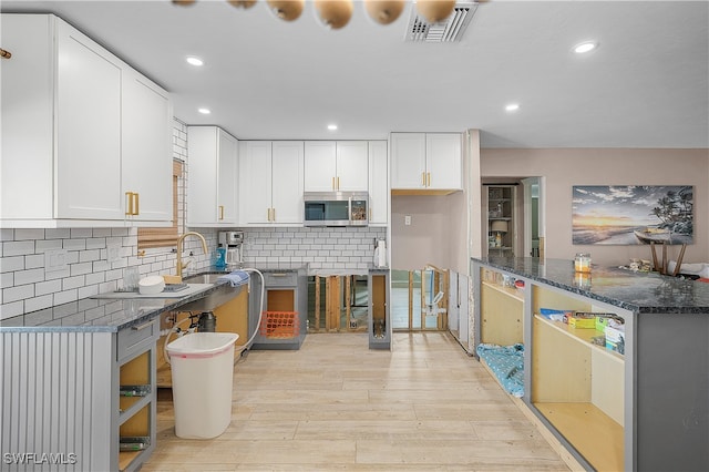 kitchen with light hardwood / wood-style floors, white cabinetry, dark stone counters, and sink