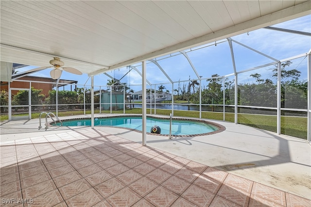 view of pool featuring a lawn, glass enclosure, a water view, ceiling fan, and a patio area