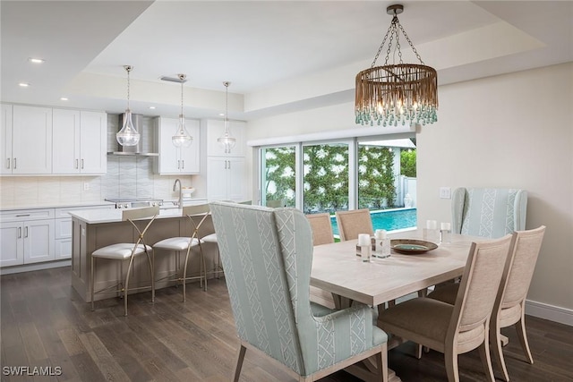 dining room with a tray ceiling, dark hardwood / wood-style flooring, a chandelier, and sink