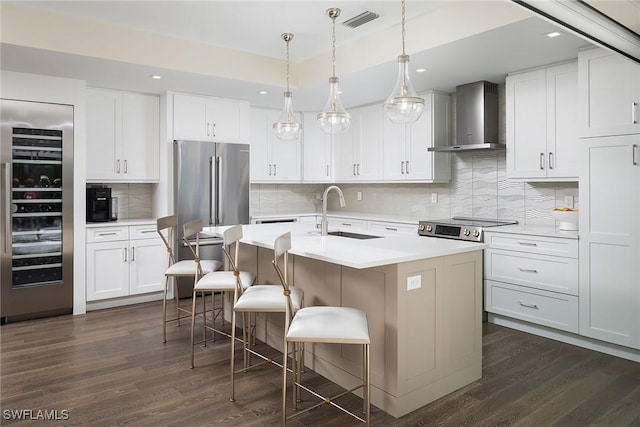 kitchen featuring a kitchen island with sink, white cabinets, a kitchen breakfast bar, sink, and wall chimney exhaust hood